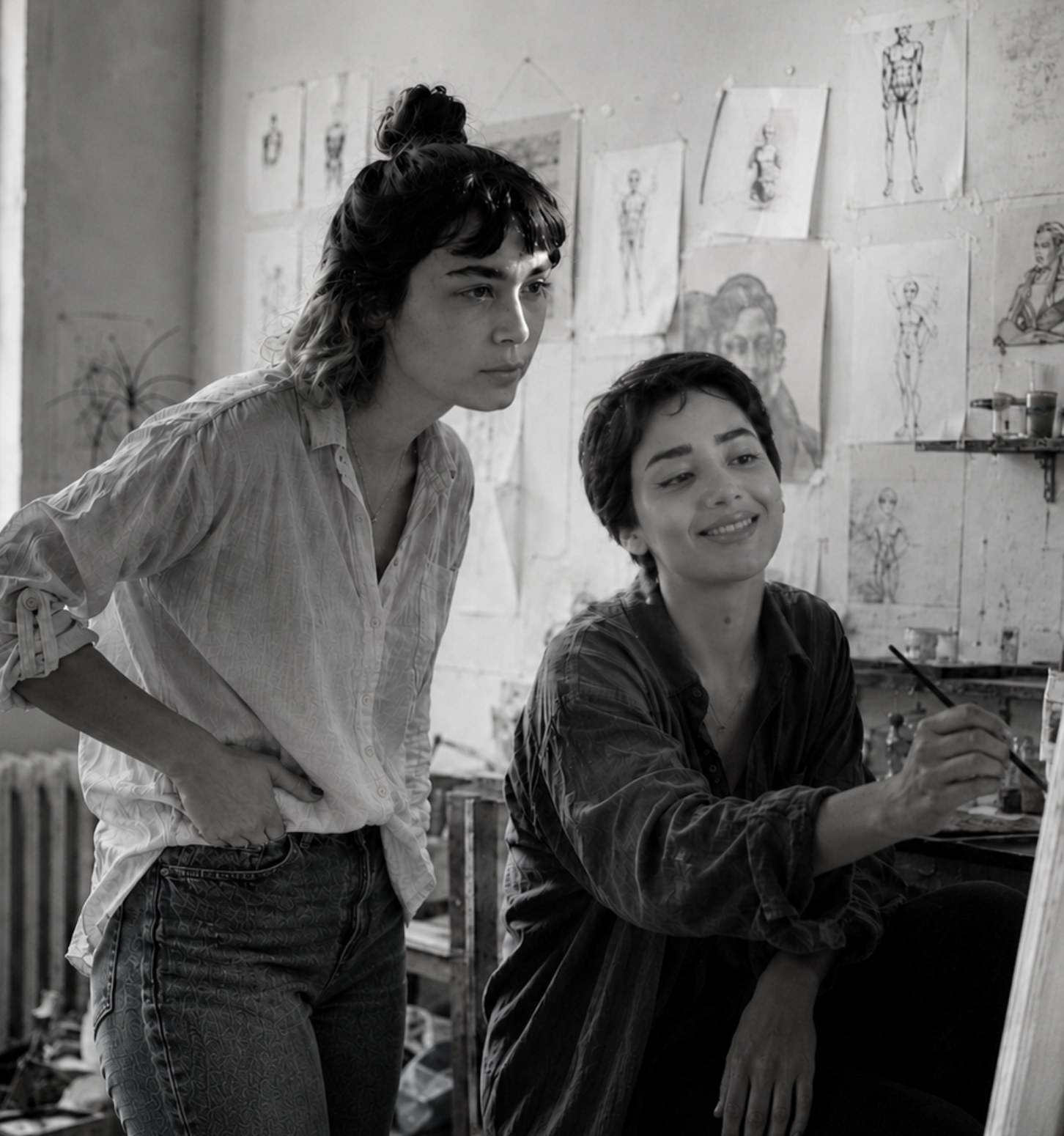 Two artists at work in the studio, one painting at an easel surrounded by figure studies